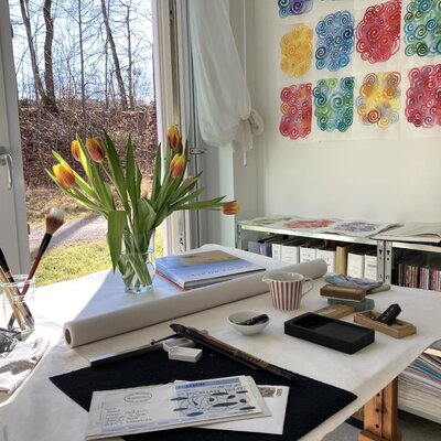 Karin Fröhlich im Studio: Blick auf meinen Arbeitstisch. Es ist Post gekommen. Das Mailart-Projekt der MYCELIA-Künstlerinnen hat begonnen. An der Wand hängen Bilder aus dem Taketori-Monogatari, dem Märchen vom Bambussammler. Japanische Mineralfarben auf Sumi-e Papier.