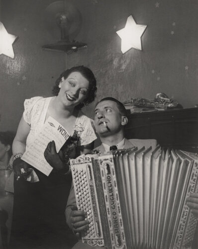 Kiki avec son accordéoniste, au Cabaret des fleurs, à Montparnasse (Kiki with her accordion player at the Cabaret des Fleurs, Rue de Montparnasse) van Brassaï, Fotografie te koop op Singulart