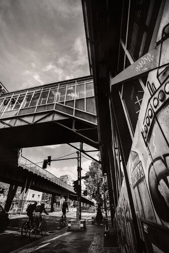 A street view in Berlin with cyclists and a train bridge in the background. di ihsan Okur, Digitale in vendita su Singulart